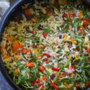 Lemon Orzo Salad with asparagus & arugula served in a black salad bowl.