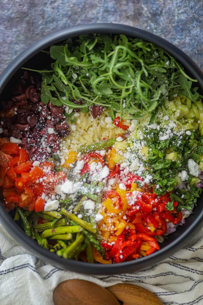 Orzo with veggies, feta cheese, and lemon vinaigreete are adding in the salad bowl.
