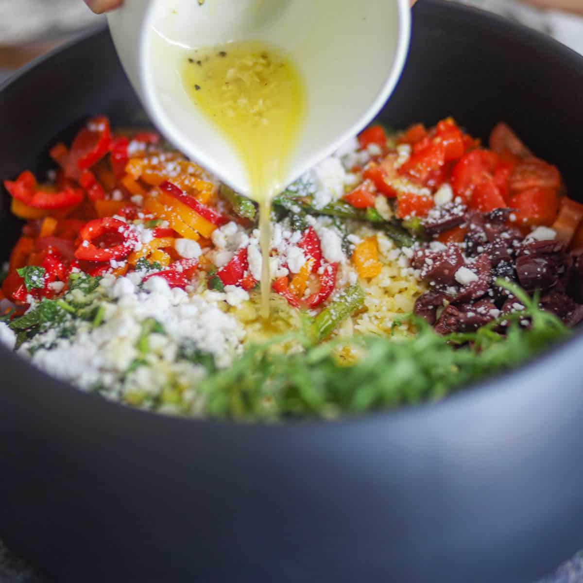 Pouring lemon vinaigrette over orzo salad.