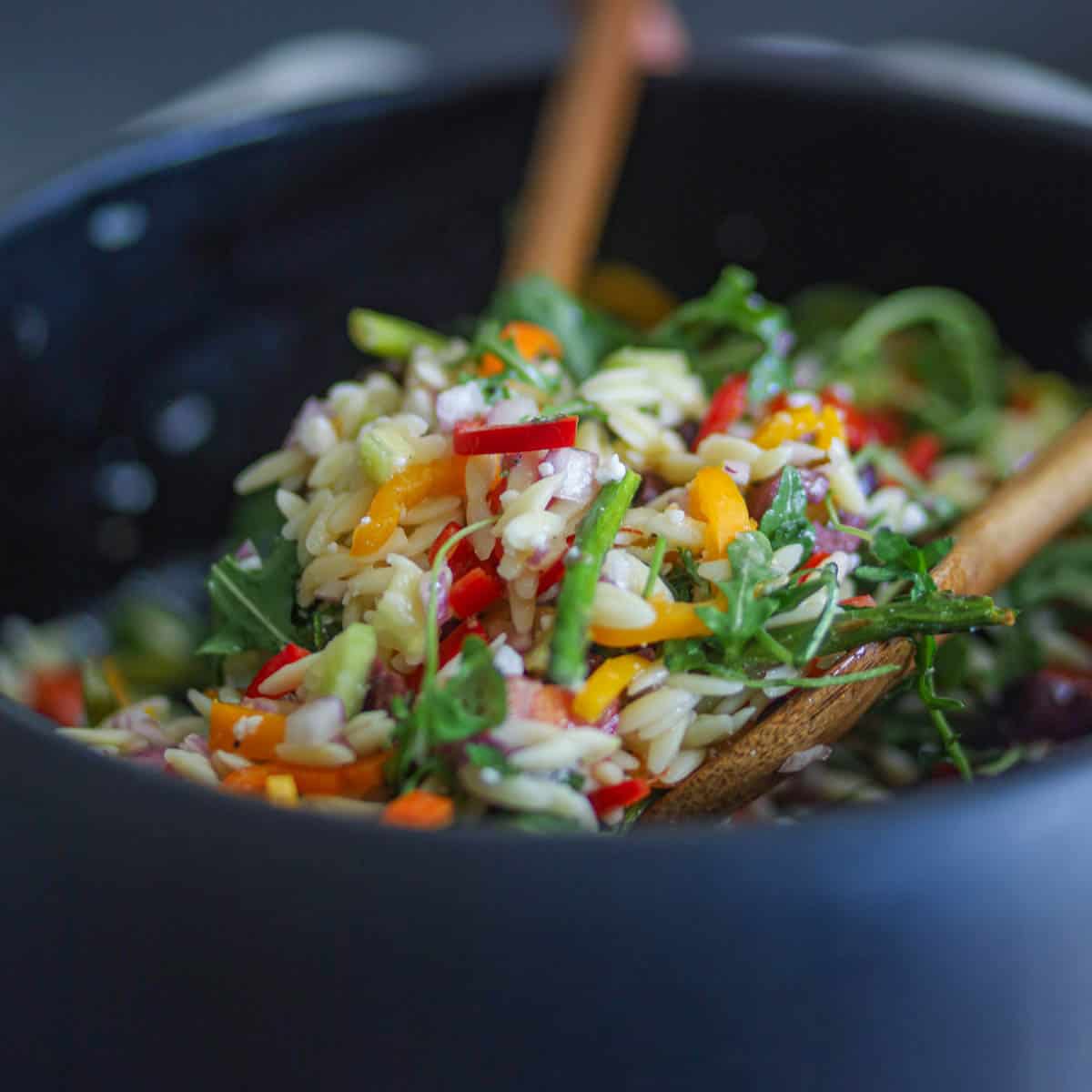Mixing the veggies with orzo using wooden spoons.