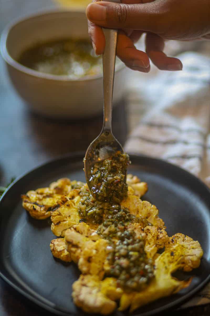 Adding a genrous layer of cilantro chimichurri sauce over cauliflower steaks.
