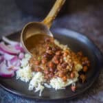 Pouring kala chana curry over rice on a black plate.