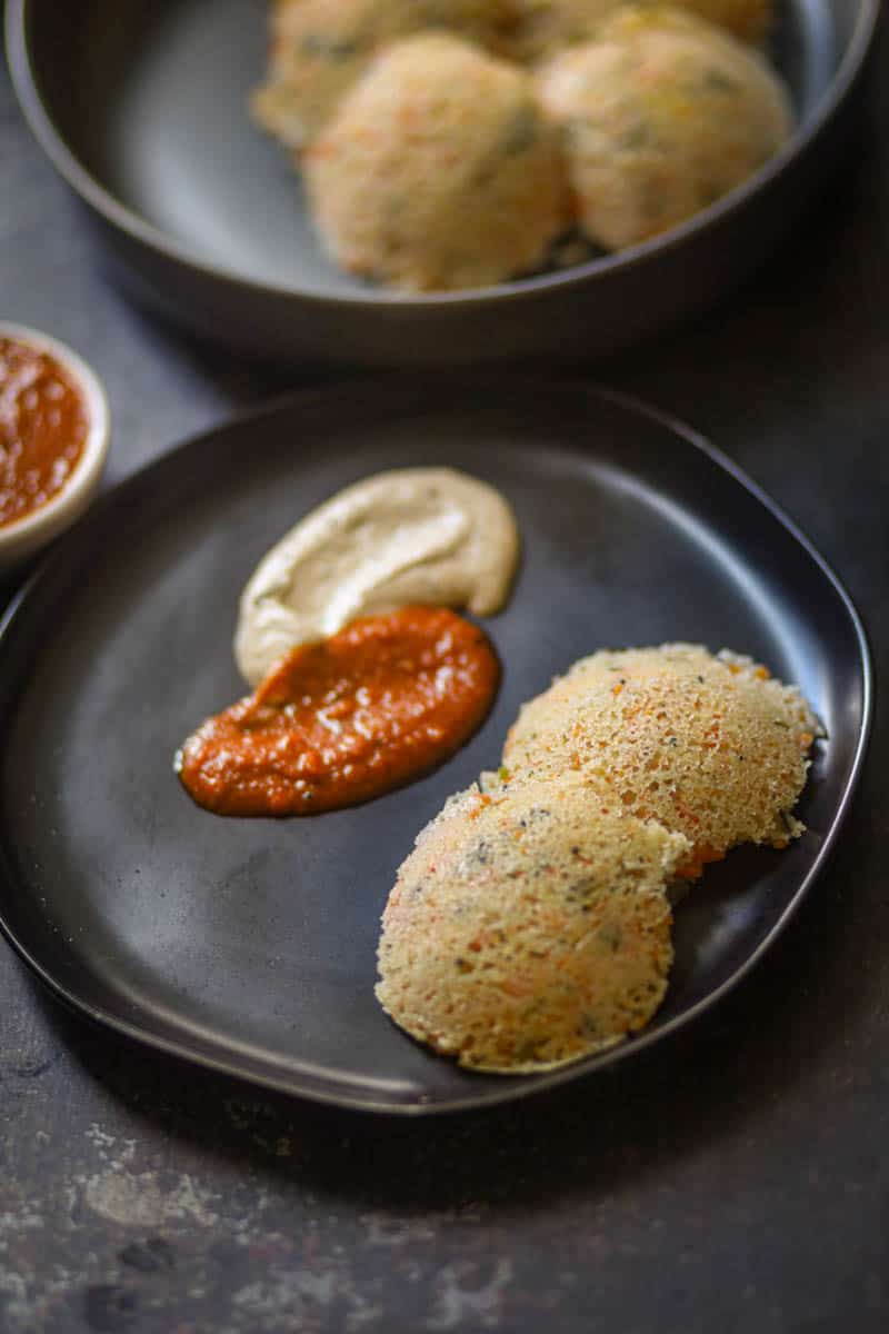 Rava Idli served with coconut chutney on a black palte.