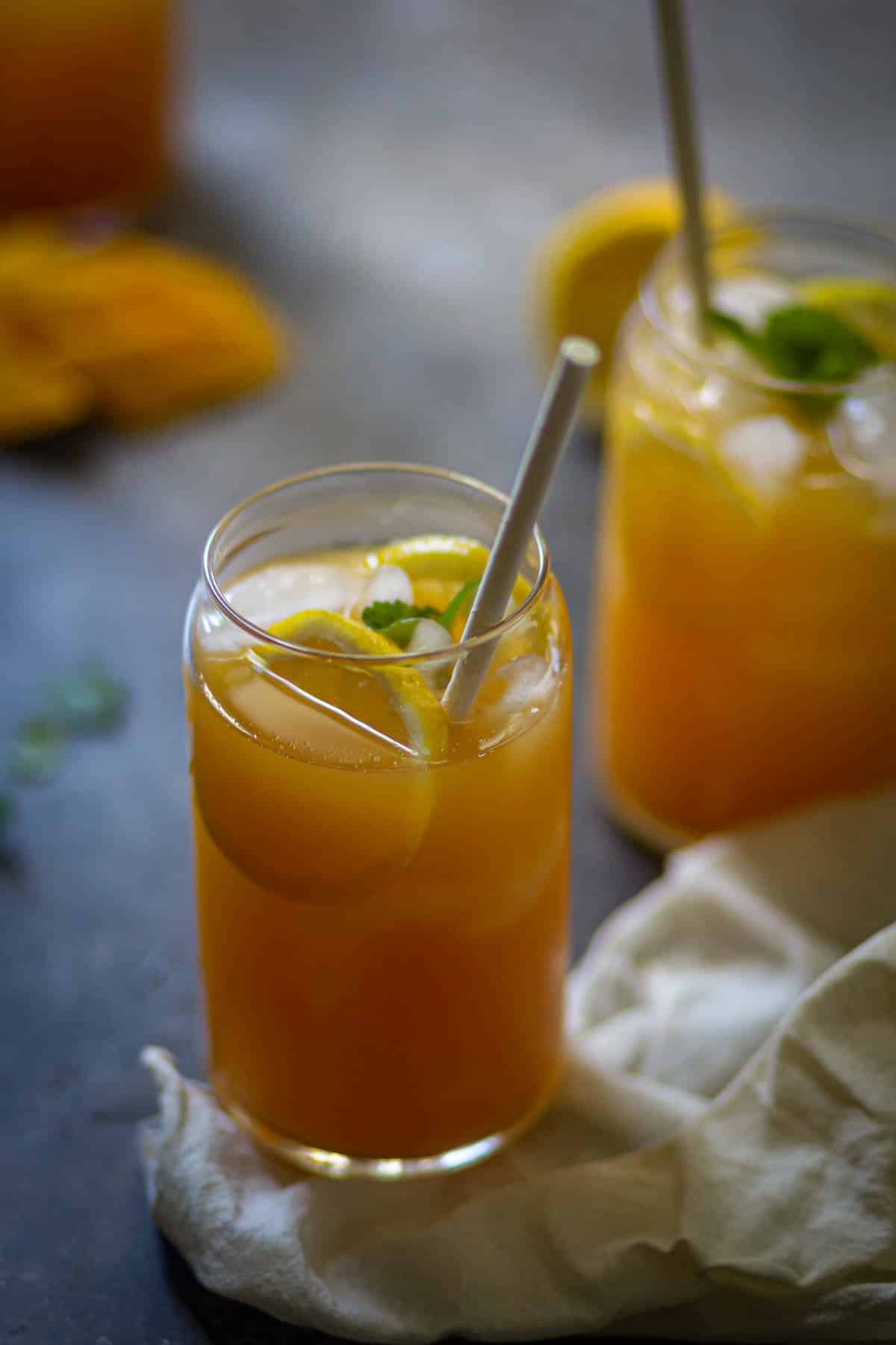Two glasses of peach mango iced tea with lemon and mint.