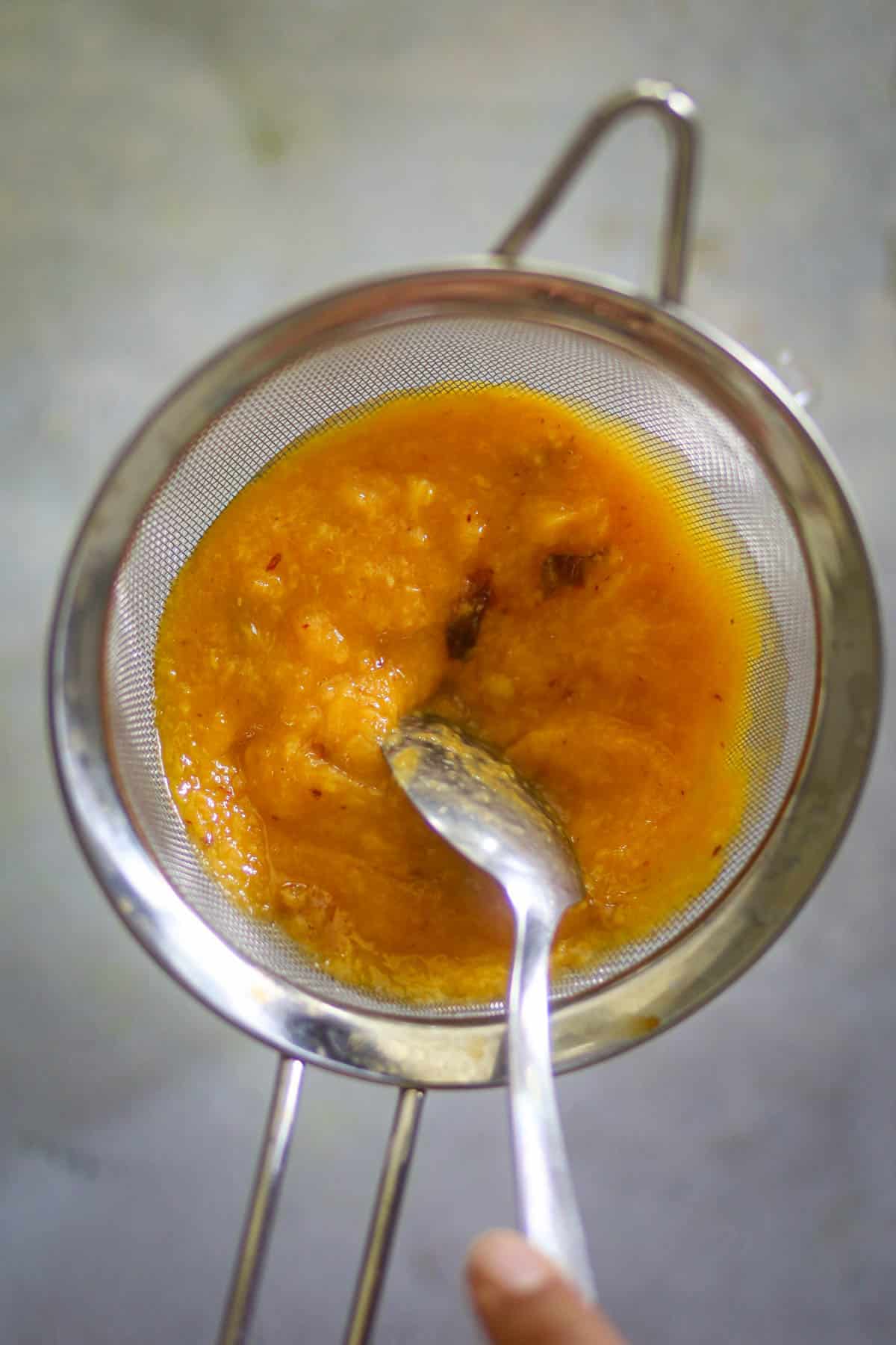 Peach and mango puree being strained through a fine-mesh strainer.