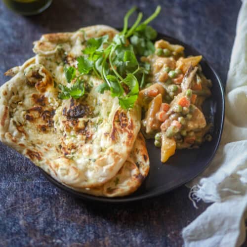 Served Navrata Curry with naan on a black plate.