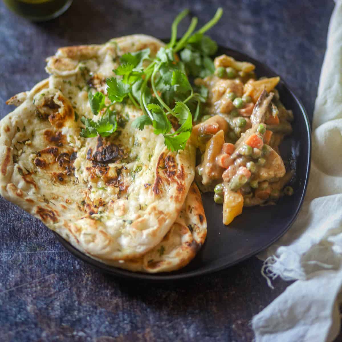Served Navrata Curry with naan on a black plate.