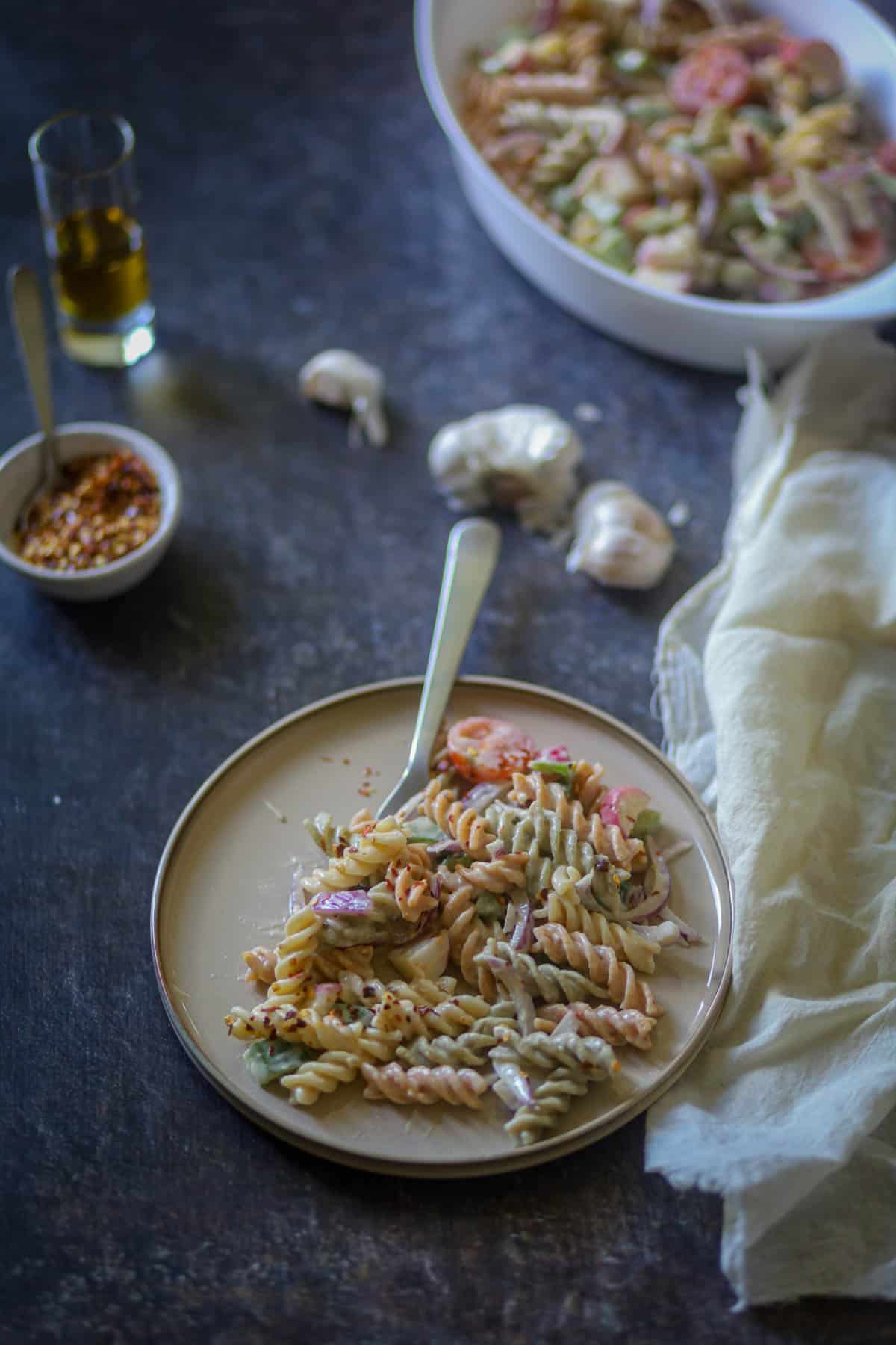 Having a tricolor pasta salad on a white plate with a fork.