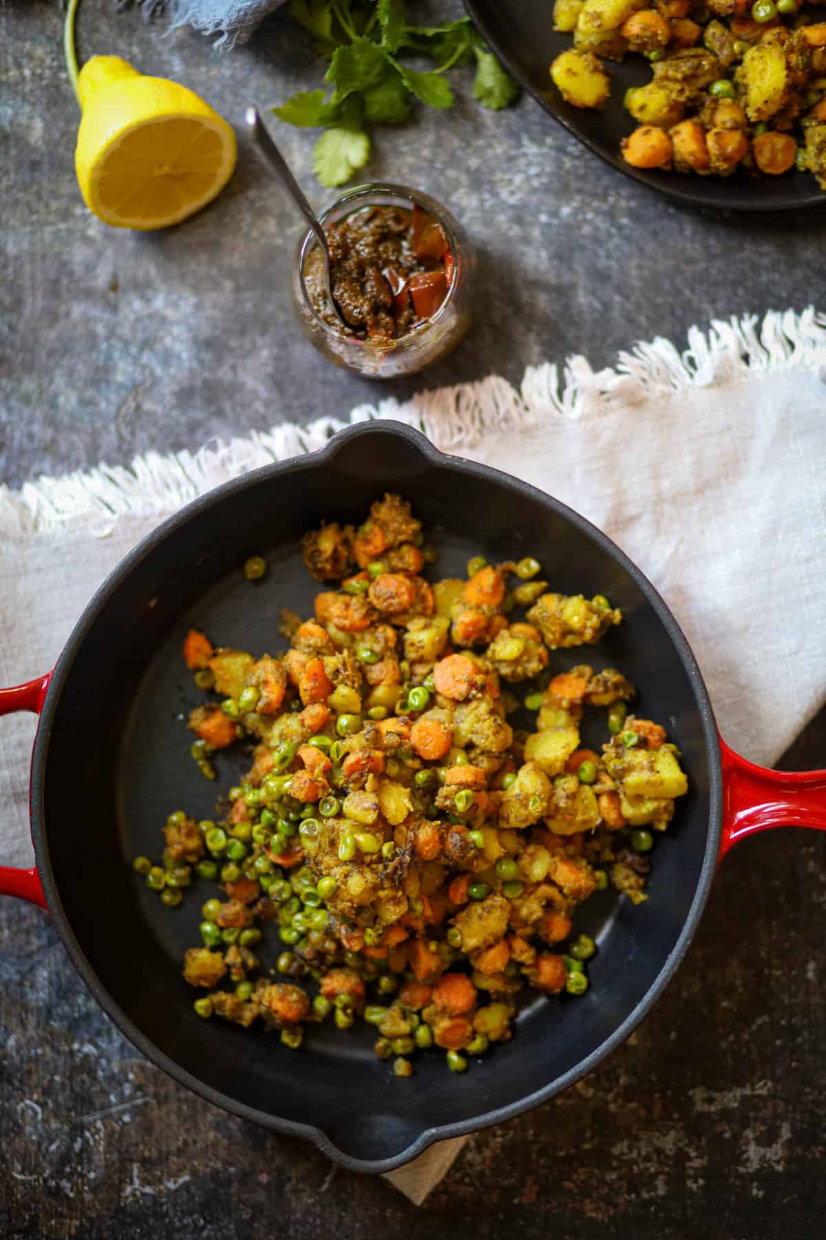 Aloo Gajar Matar serve din a red skillet with pickle on the side.