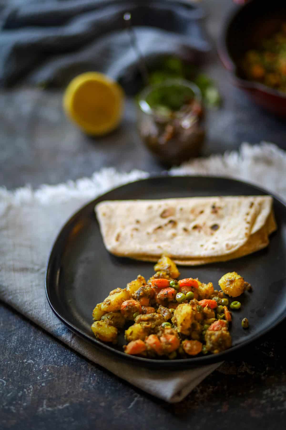 Aloo Gajar Matar with roti on a black plate.