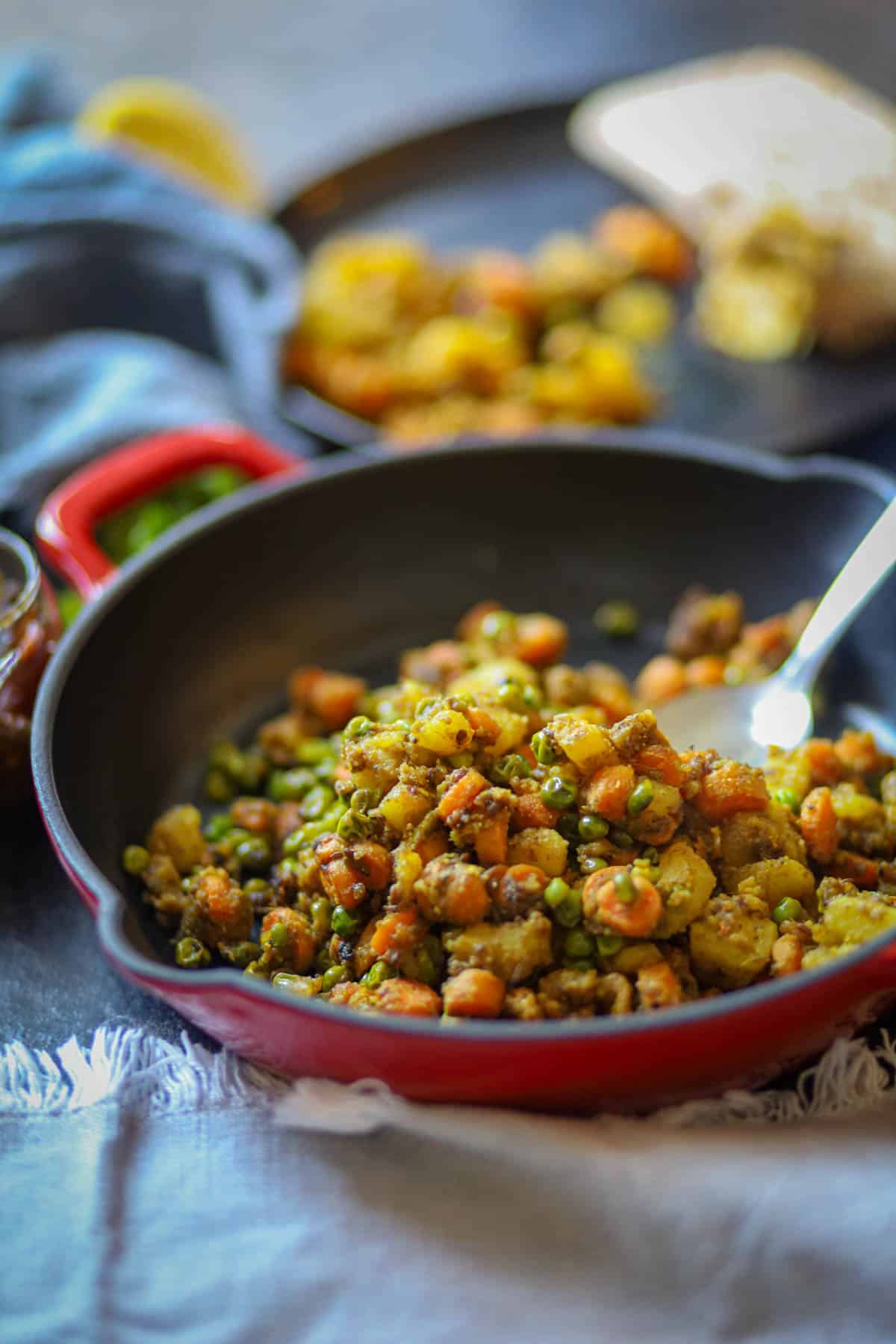 Aloo Gajar Matar serve in a red skillet with a spoon.