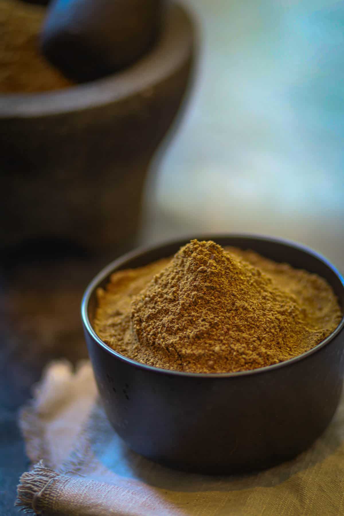 A big mountain of garam masala in a black bowl.