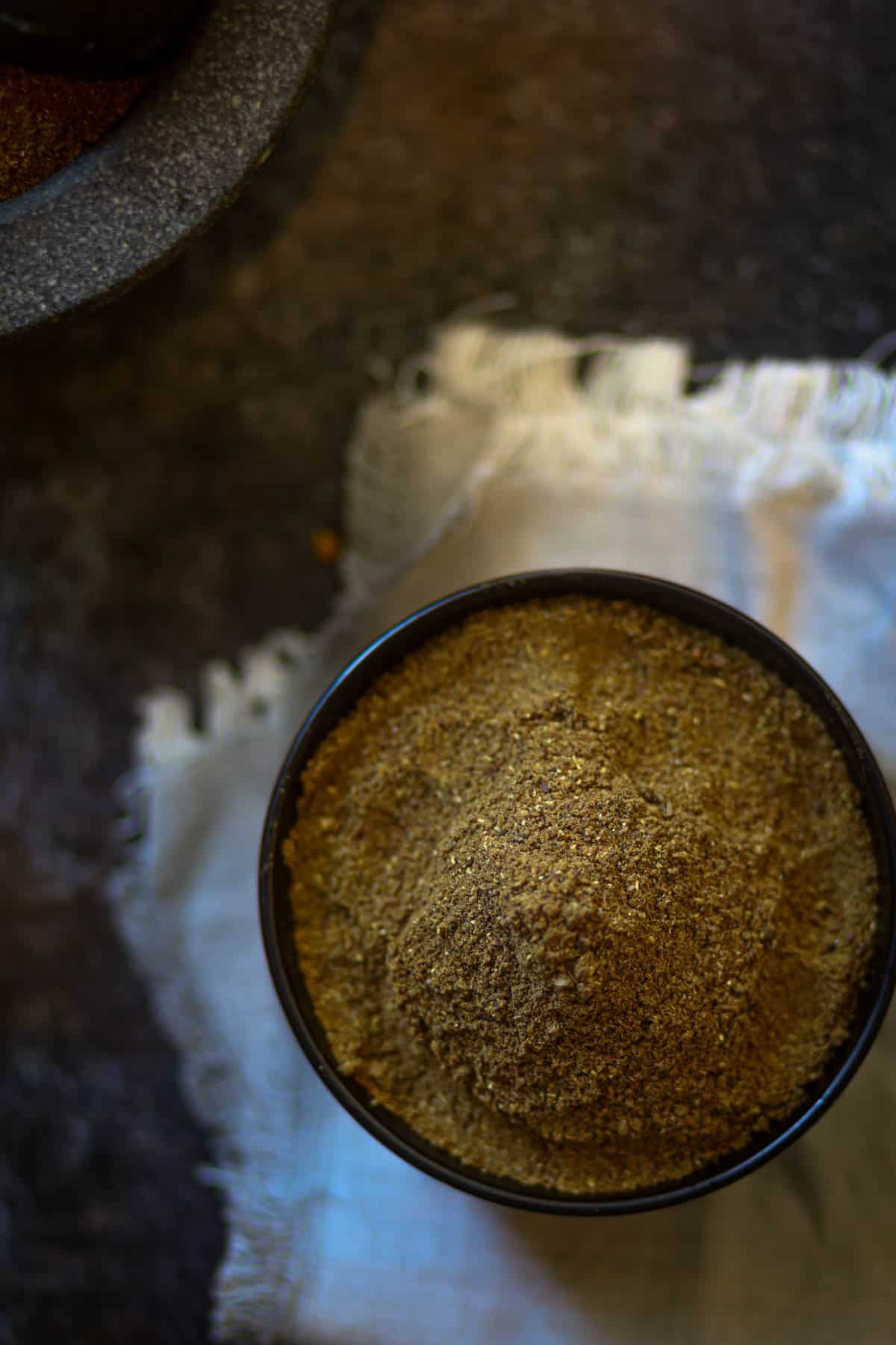 Overshot of garam masala in a black bowl over a white cloth.