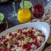 Image of rice with pomegranate seeds with ghee, pomegranate seeds, and lime on the side.