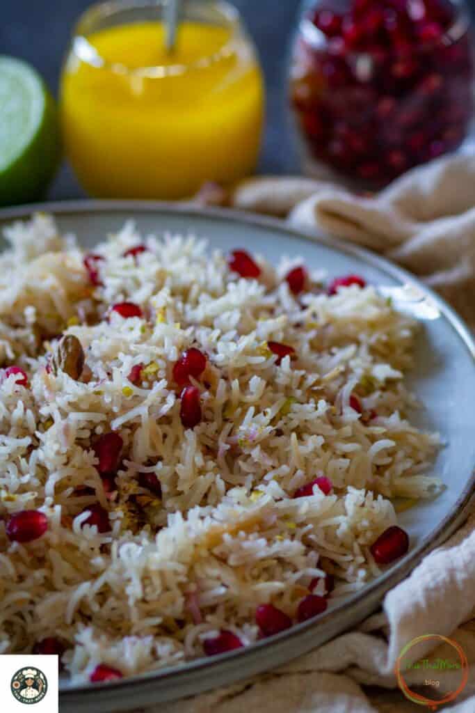 Image of a big plate filled with pomegranate rice which is garnished with fresh pomegranate seeds and pistachios.