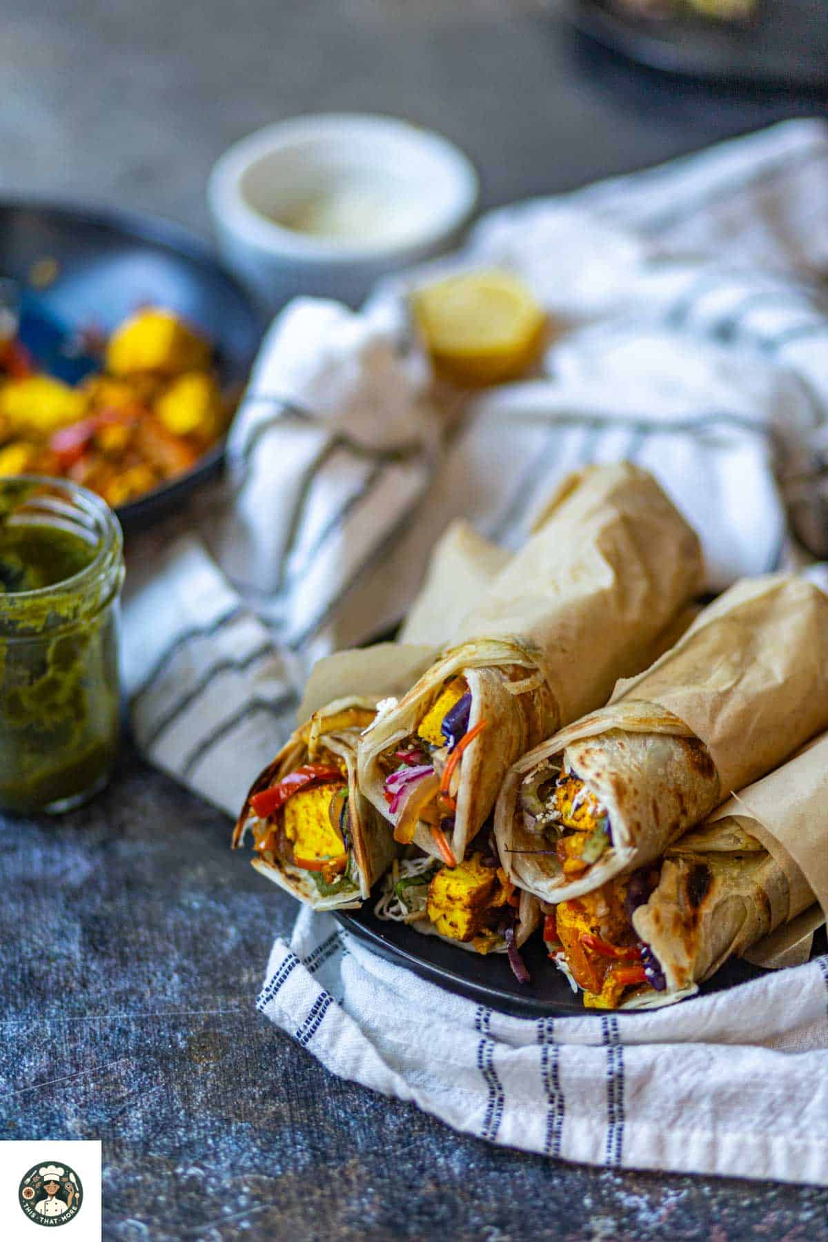 Sideshot of paneer kathi roll on a black plate served with green chutney.