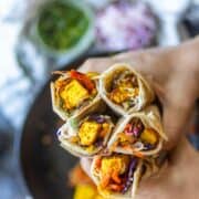 Overshot image of a hand holding 5 paneer kathi rolls.
