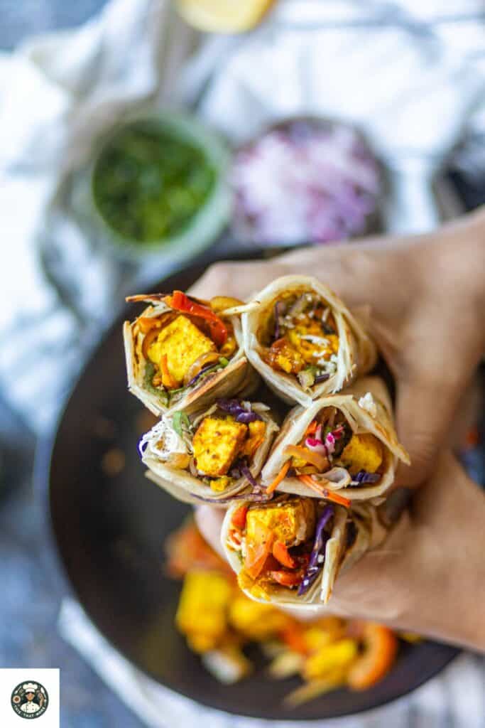 Overshot image of a hand holding 5 paneer kathi rolls.