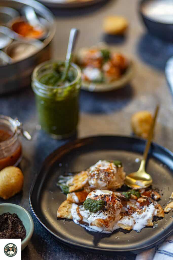 A sideshot of dahi bhalla recipe serve don a black plate with chutneys placed on the side.