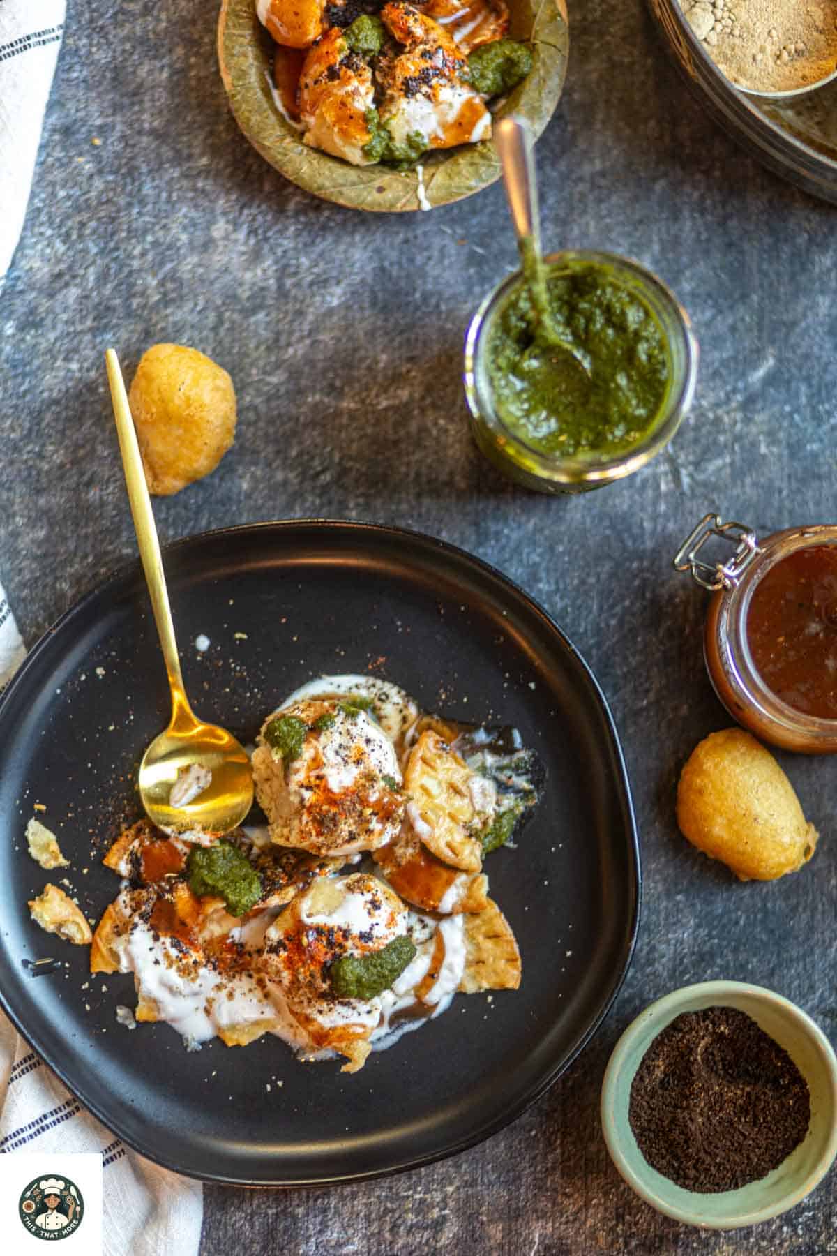 Overshot of Dahi Vada Chaat on a black plate with golden spoon placed on the side.