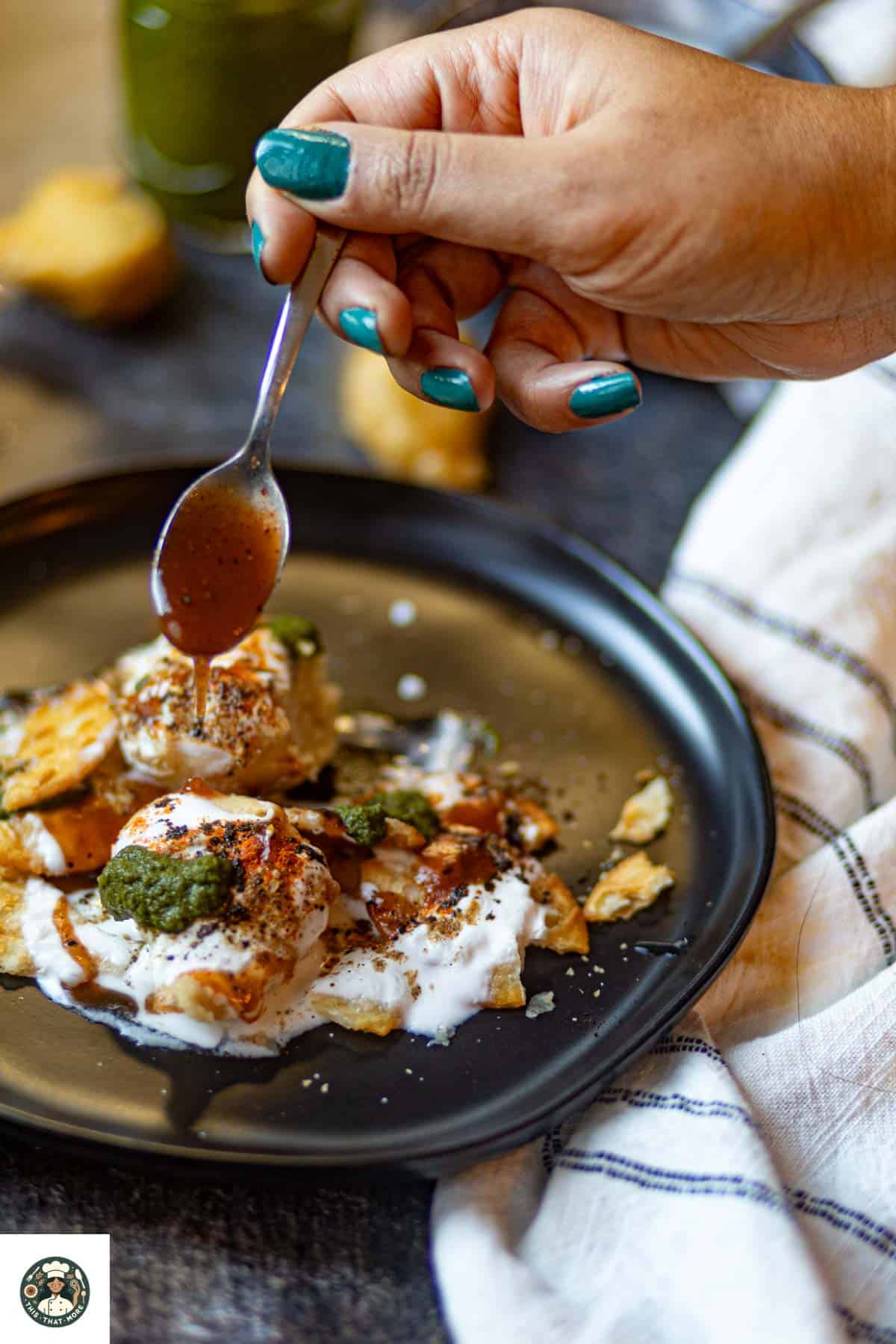 Image showing a spoonful of tamarind chutney added to the bhalla chaat.