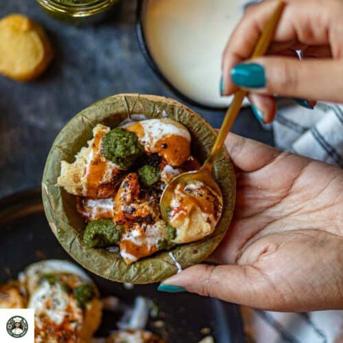 A small bowl filled with dahi bhalla chaat placed in the palm.
