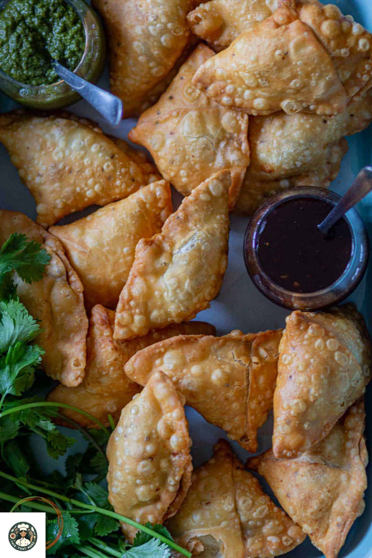 Overshot image of plenty of samosas served in a tray with tamarind chutney and garnished with cilnatro.