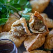 Image of a half-cut Punjabi samosa over a whole lot of samosas with tamarind chutney on the side.