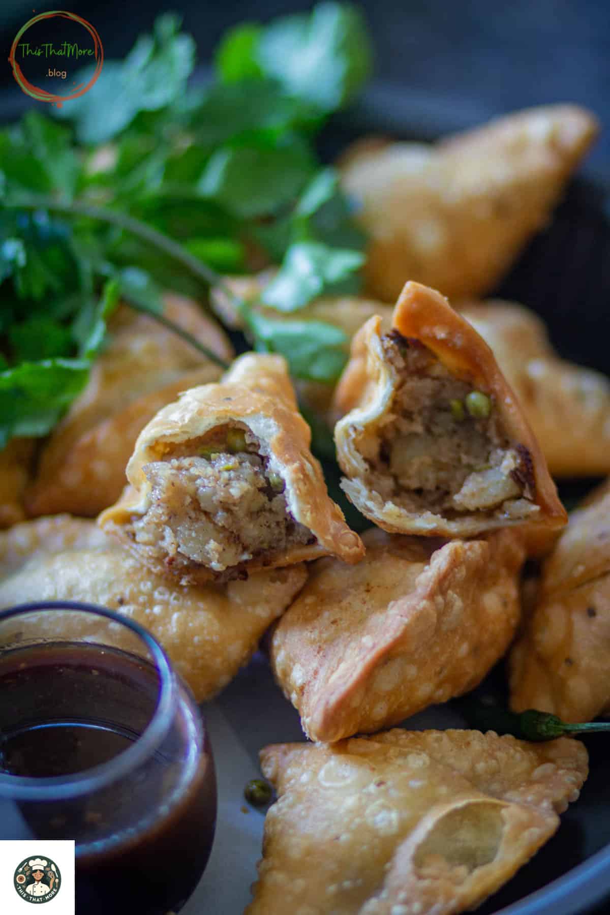 Image of a half-cut Punjabi samosa over a whole lot of samosas with tamarind chutney on the side.