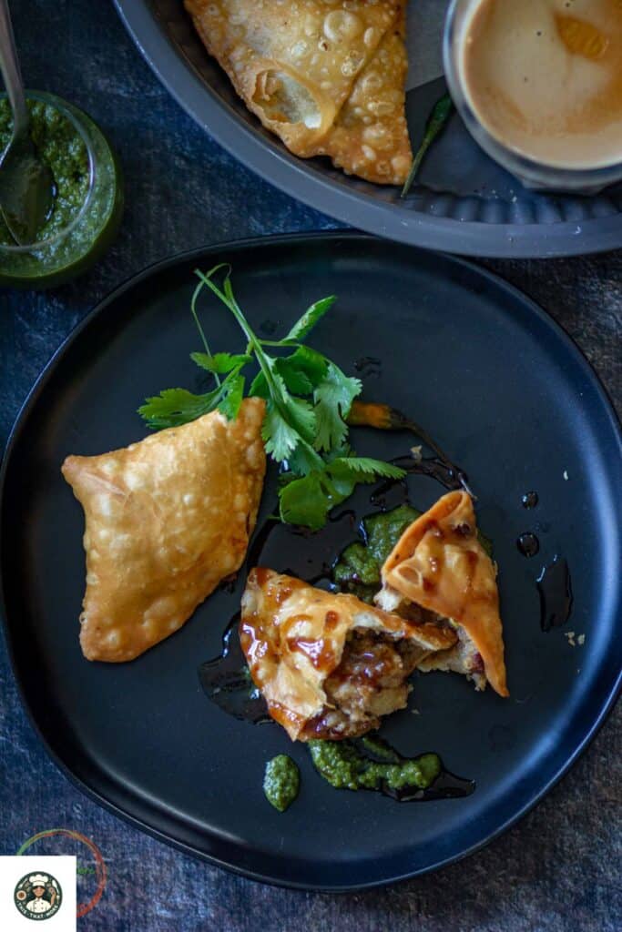 Image of punjabi samosa served on a black plate with tamarind and green chutney.