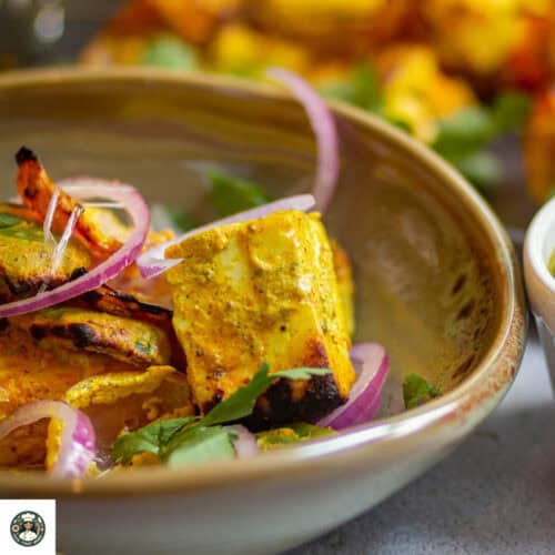 Featured image of tandoori paneer tikka served in a olive green bowl with sliced onions.