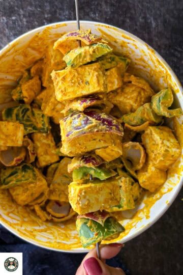 Image showing alternating the onion, bell peppers, and paneer in a steel skewer for making paneer tikka.