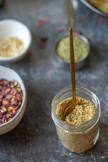 Image showing thandai masala in a mason jar with the golden spoon.