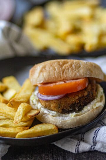 Aloo Tikki Burger served with potato fries on a black plate.