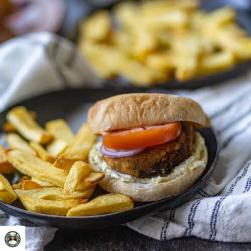 Aloo Tikki Burger served with potato fries on a black plate.