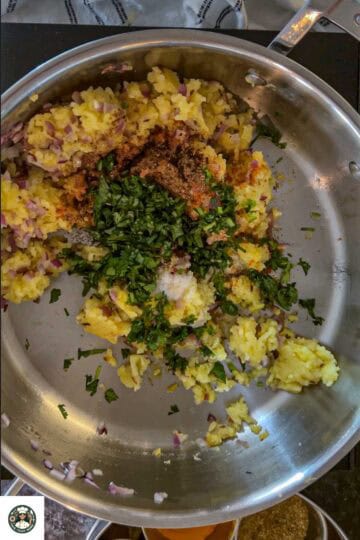 Next, add spices, cilantro, and soaked poha to the potatoes.