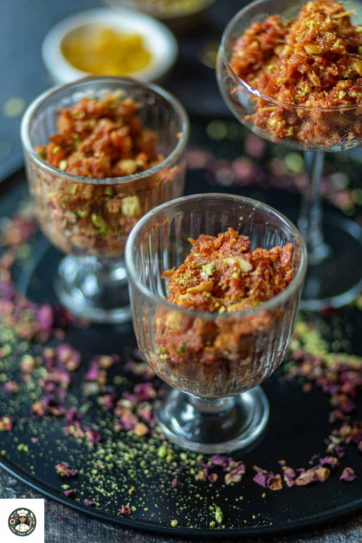 Carrot halwa served in glass dessert cups on a black plate.