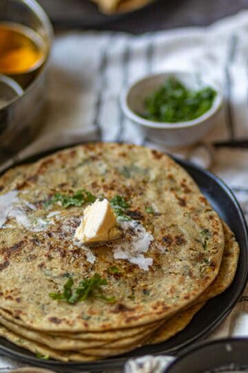 Image showing dollop of butter added to stack of gobi parathas.