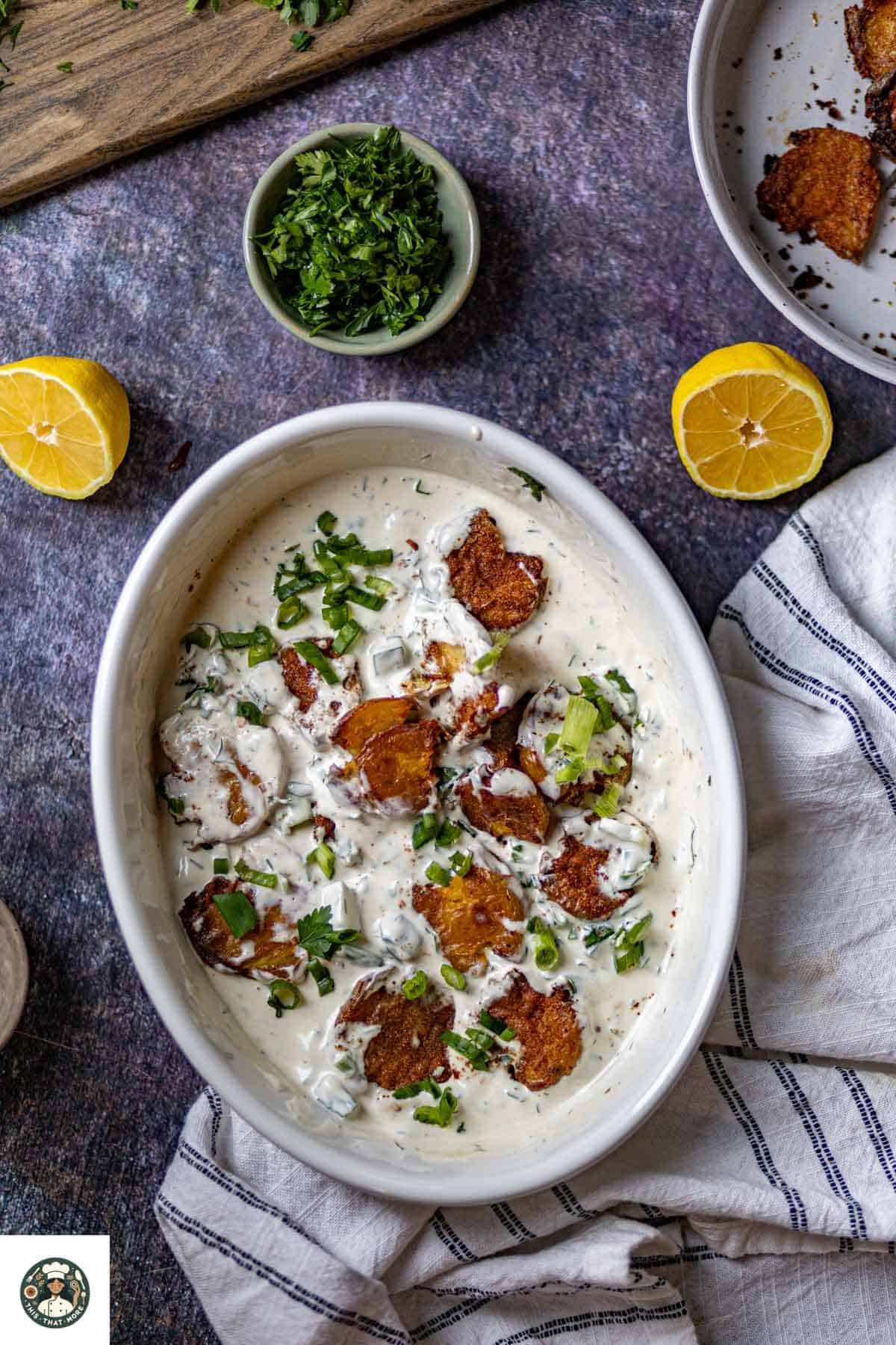 Overshot of smashed baby potatoes salad served in a white bowl in creamy yogurt dressing.