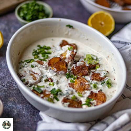 A white bowl with potatoes and green onions
