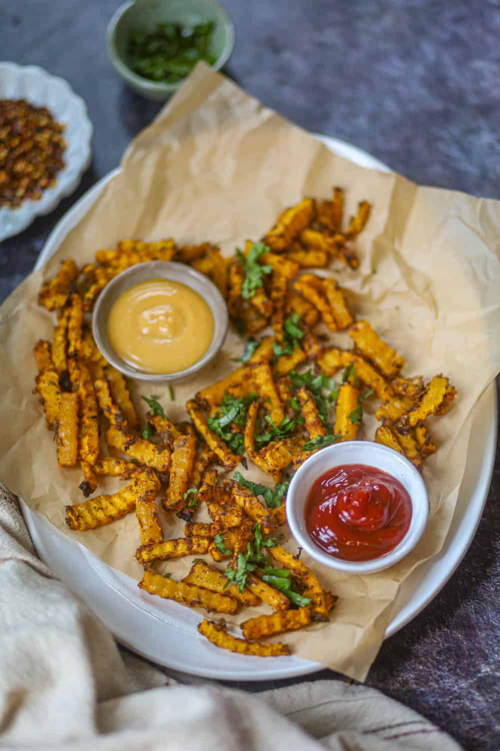 Air fryer butternut squash fries served with ketchup and creamy dipping sauce on a parchment-lined plate.
