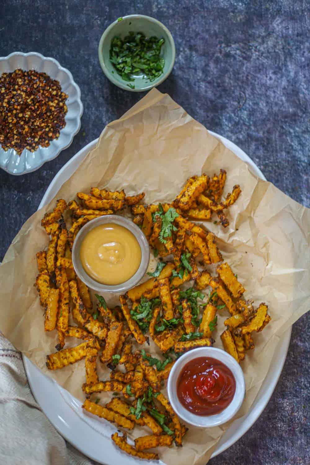 Air fryer butternut squash fries served with ketchup and creamy dipping sauce on a parchment-lined plate.