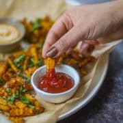 Hand dipping a crispy air fryer butternut squash fry into ketchup