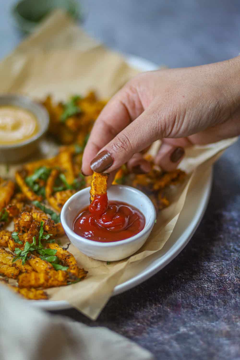 Hand dipping a crispy air fryer butternut squash fry into ketchup