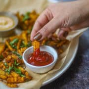 Close-up of dipping air fryer butternut squash fry into ketchup on a plate of crispy fries.