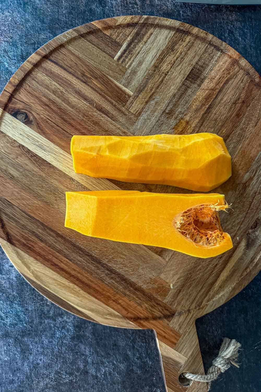 Peeled butternut squash cut in half on a wooden cutting board.