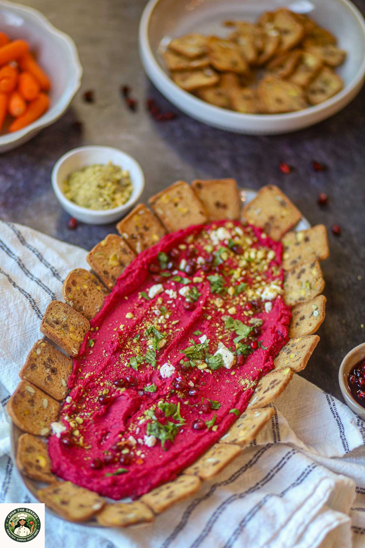 Beetroot hummus platter served with whole grain crackers and toppings.
