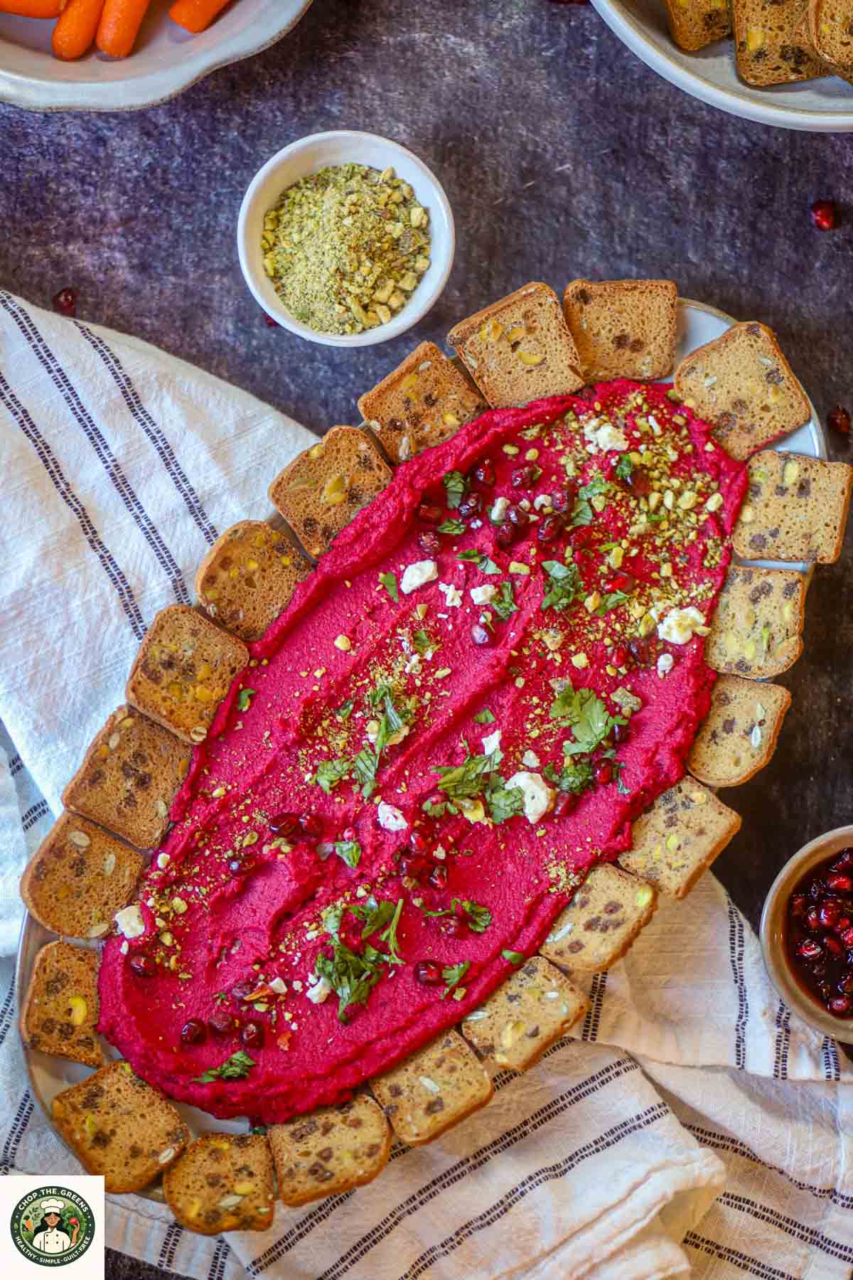 Overhead view of beetroot hummus served with crackers and toppings.