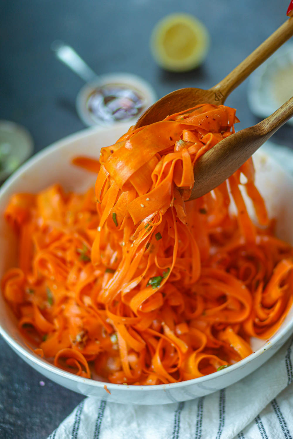 Wooden tongs lifting carrot ribbons from the salad bowl.