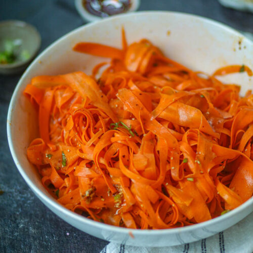Fresh carrot ribbon salad in a white bowl with herbs and light dressing.